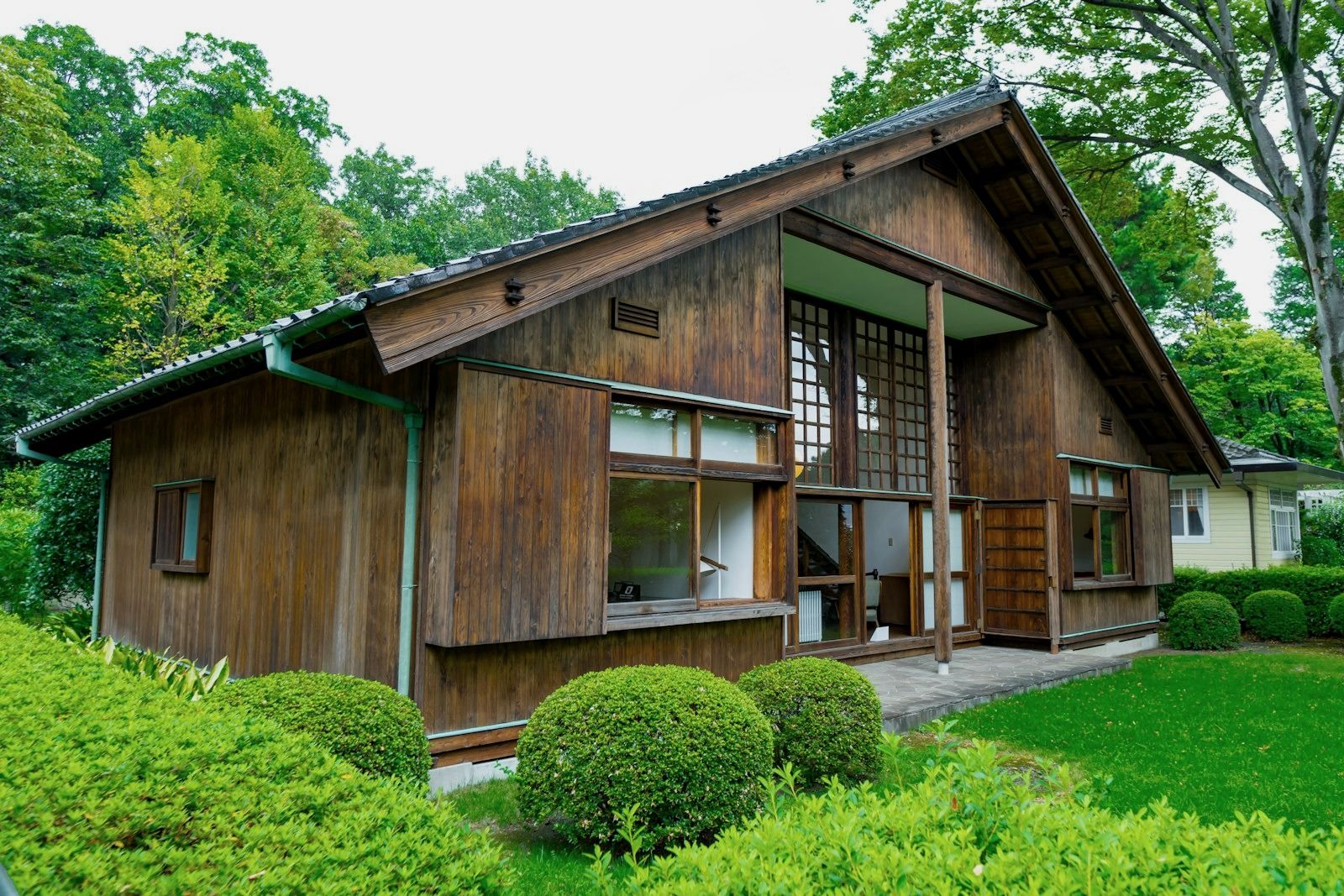 緑の庭に面した、木の外壁と大きな窓の平屋